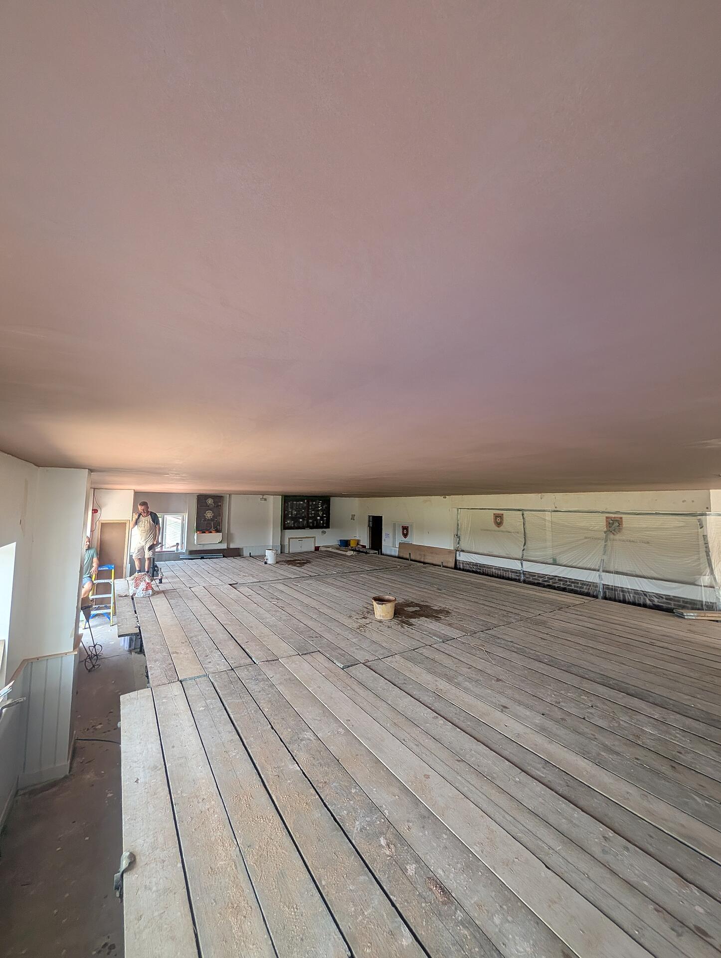 Finished clubhouse ceiling running unbroken across the full width of the function room, honour boards masked below