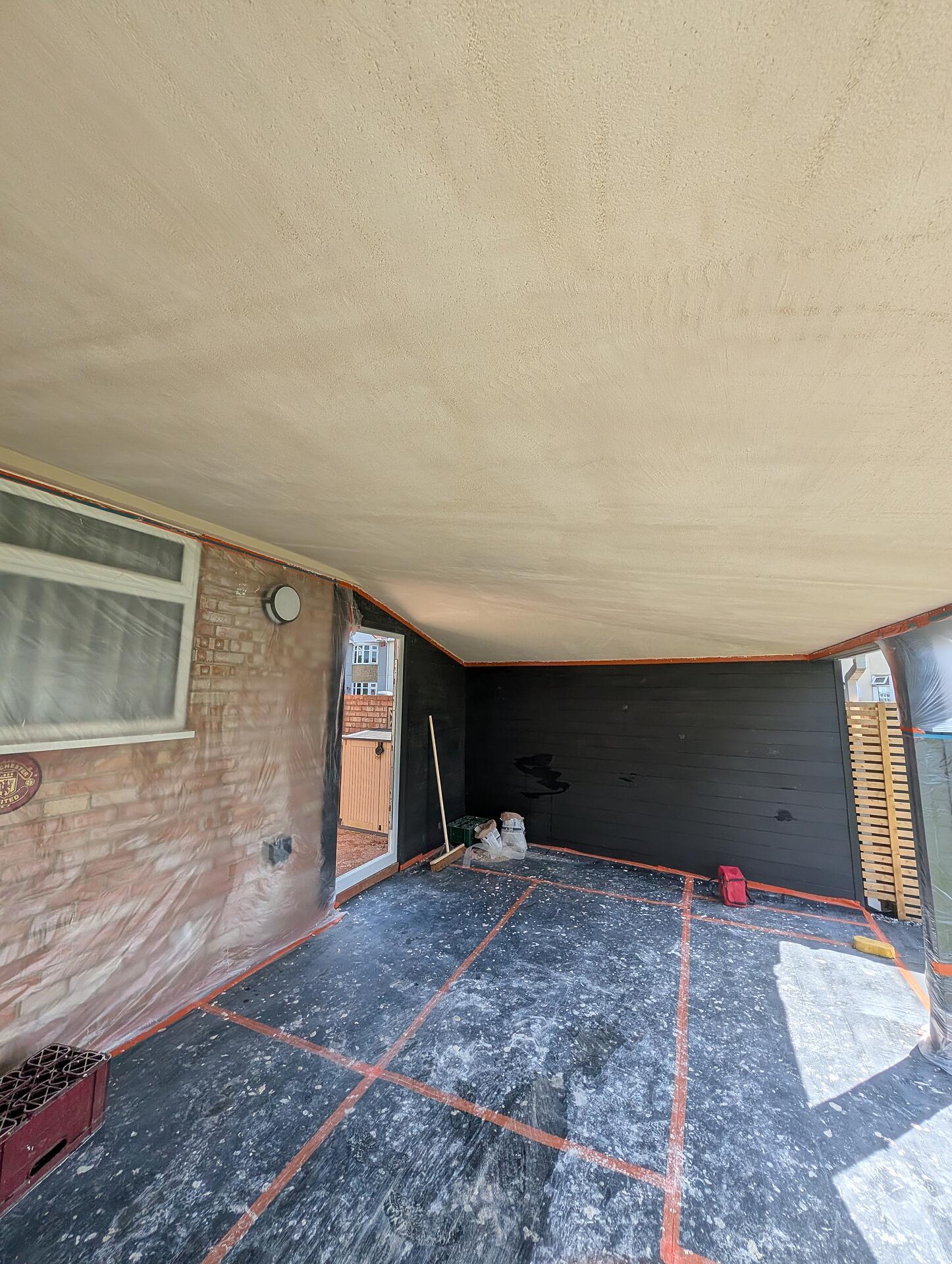 Outdoor canopy ceiling finished in textured render above black cladding, the floor still masked and taped