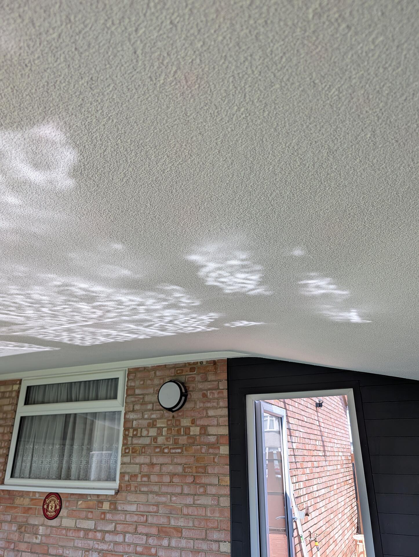 Textured render finish on a garden canopy ceiling, dappled sunlight picking out the even grain