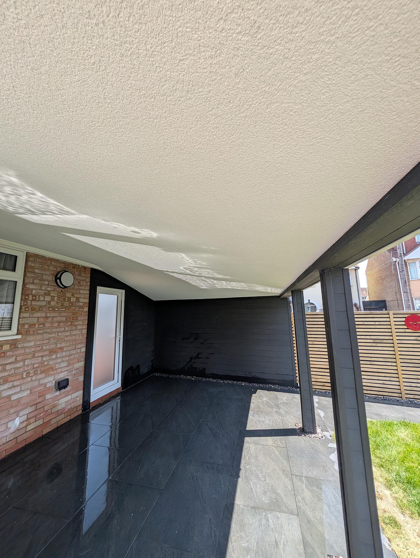 Completed outdoor room, its rendered ceiling meeting black cladding above a wet slate floor