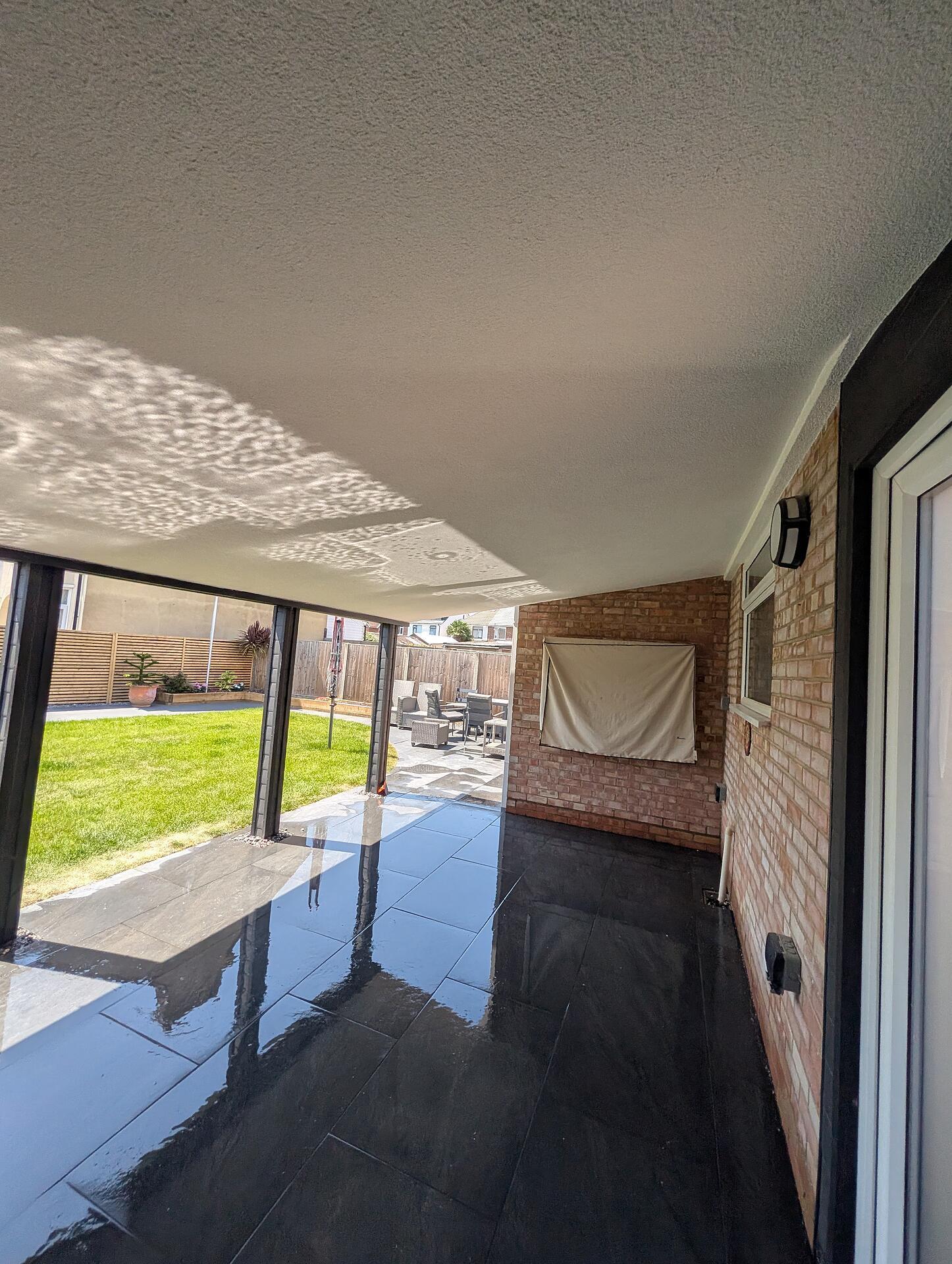 Finished covered terrace looking out over the lawn, the rendered ceiling clean to the edge above slate paving
