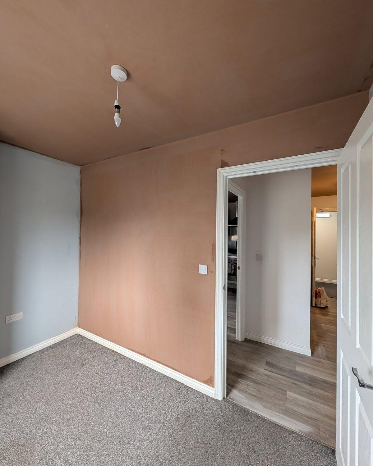 Room with smooth, freshly skimmed walls and ceiling, open through to the hallway beyond