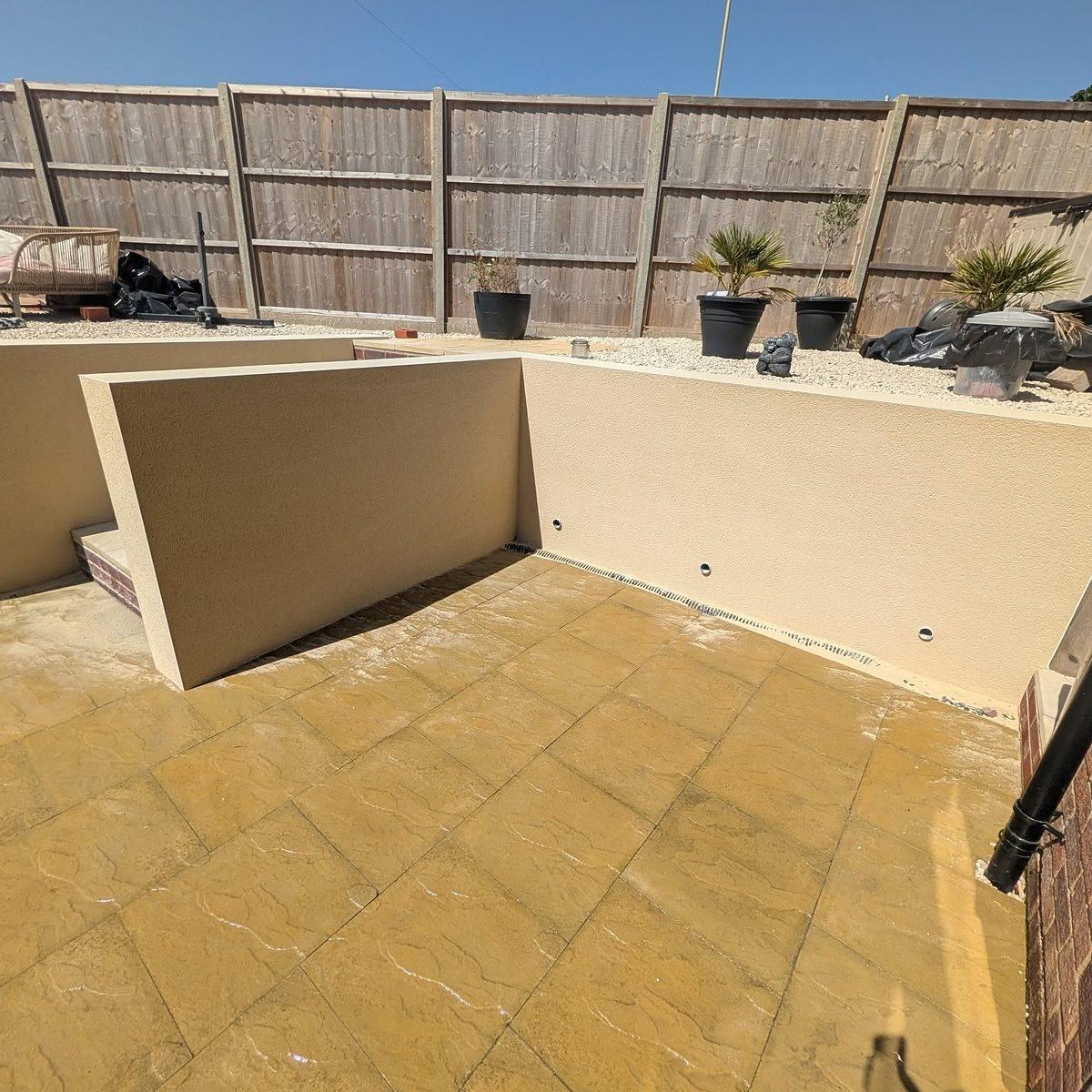 Rendered garden wall corner in a cream finish, with planters and new paving in bright sun
